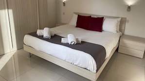 A neatly made bed with white linens and a red pillow, a bedside table, and a wardrobe with a light wood finish. - Stylish 2BR Meridian suite in central St Julians (San Ġiljan)
