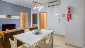 A modern living room with a sofa, dining table, and chairs. There is a television, a fireplace, and a ceiling light fixture. - Stylish 2BR Meridian suite in central St Julians (San Ġiljan)