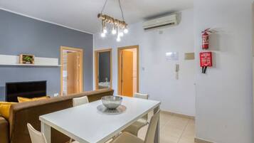 Una sala de estar moderna con un sofá, una mesa de comedor y sillas. Hay un televisor, una chimenea y una lámpara en el techo.