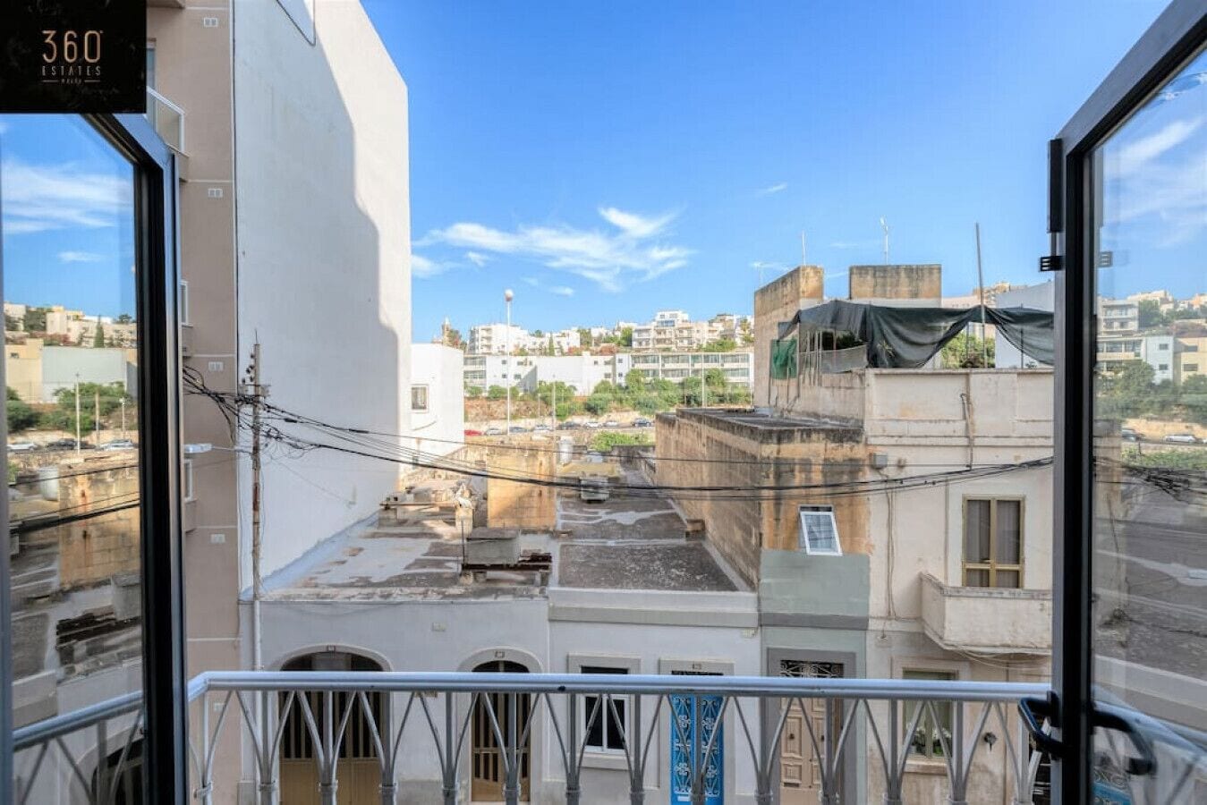 Vista desde un balcón sobre un paisaje urbano con edificios, líneas eléctricas y cielo despejado.