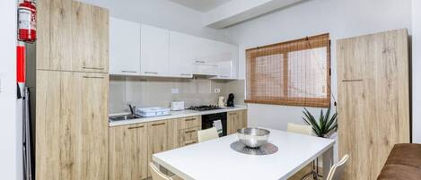 A modern kitchen with white cabinets, a dining table, and a fire extinguisher.