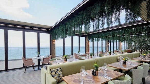An outdoor dining area with tables and chairs, overlooking the sea.