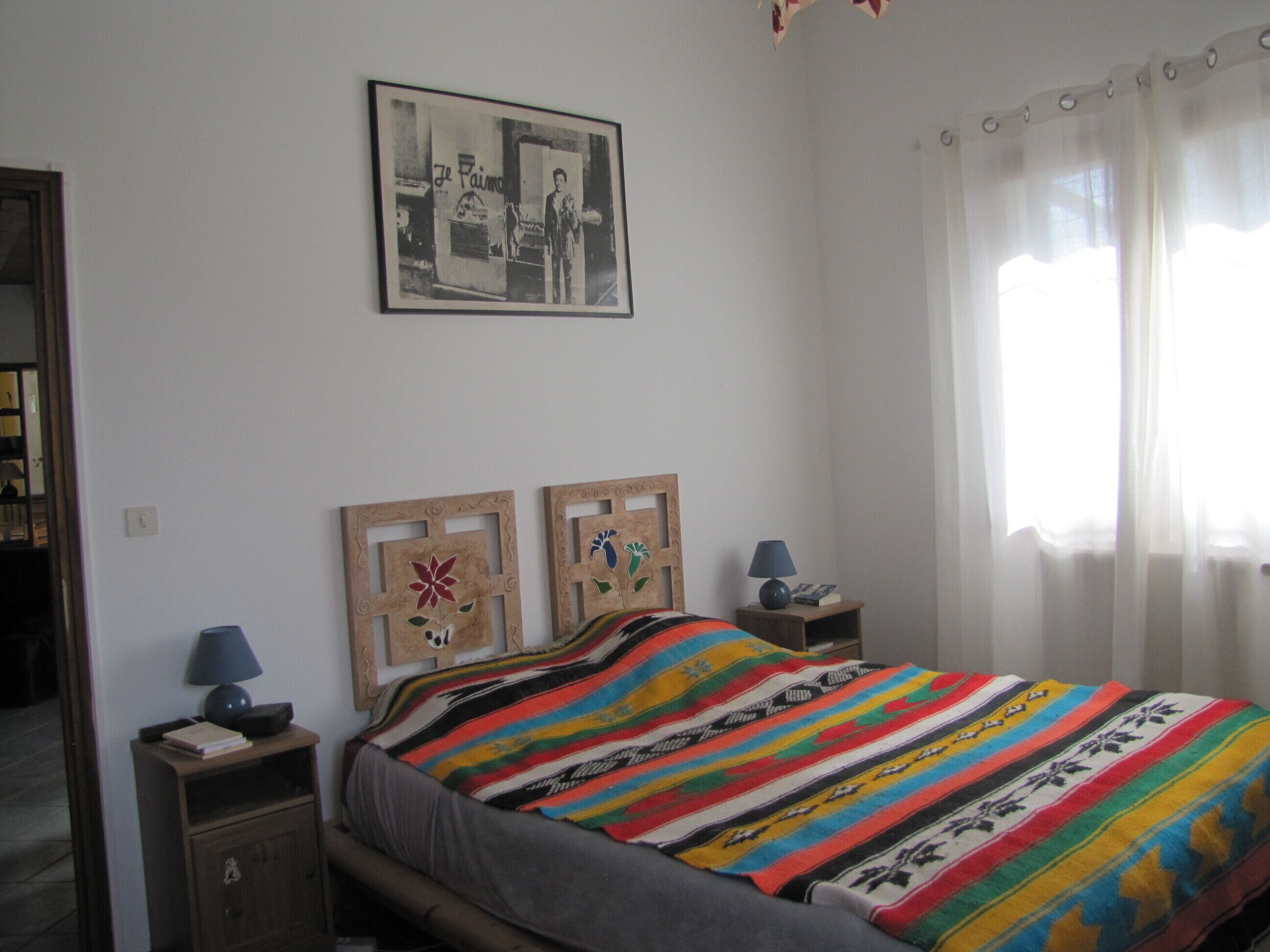 A bedroom with a bed, two nightstands, a lamp, a framed picture on the wall, and a window with curtains.