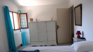 Ein Schlafzimmer mit einem Bett, einem Kleiderschrank, einem Nachttisch mit Lampe und einem Fenster mit Vorhängen.