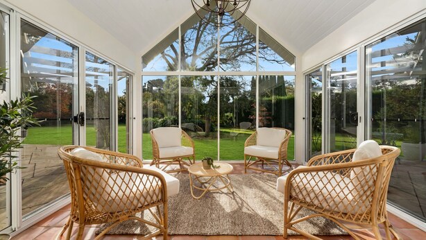 A conservatory with a glass ceiling, wicker furniture, and a view of a well-maintained garden. - Hollydale, Burradoo, Southern Highlands (Burradoo)
