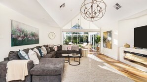 A spacious living room with a sectional sofa, a fireplace, and a large window offering a view of the outdoors. - Hollydale, Burradoo, Southern Highlands (Burradoo)