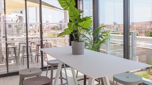 A modern indoor space with a white table and stools, a large potted plant, and large windows offering a city view. - Apparthôtel Privilodges Toulon Centre Gare (Toulon)