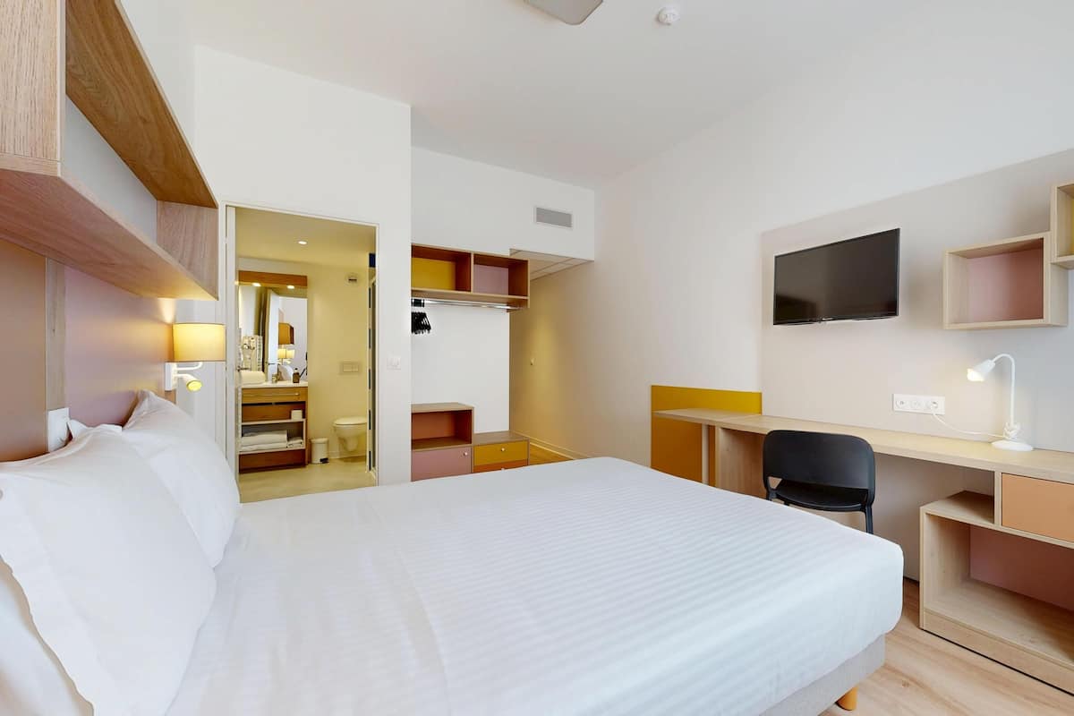 Une chambre d’hôtel avec un lit, un bureau, une chaise, une télévision et un miroir.