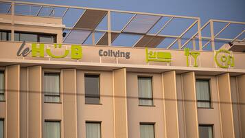 A building with a sign that reads "le HUB Coliving" and icons indicating amenities such as a bed, a fork and knife, and a circular icon.