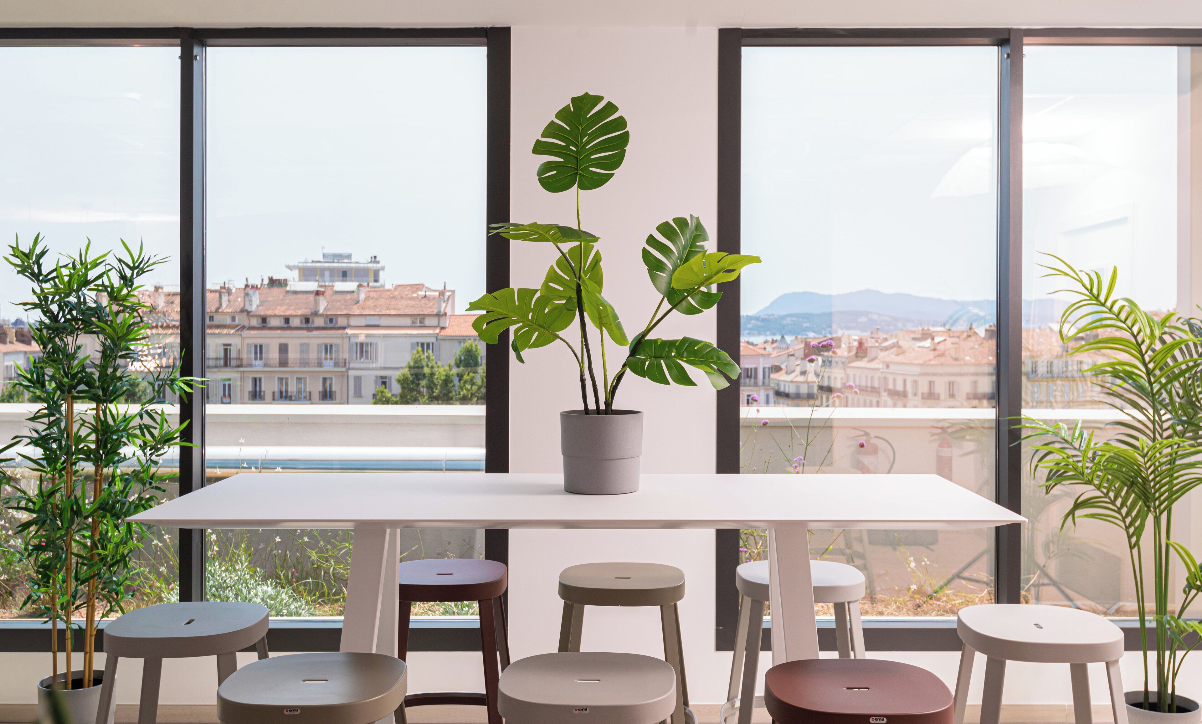 Ein moderner Raum mit großem Fenster, einem weißen Tisch und mehreren Hocker.