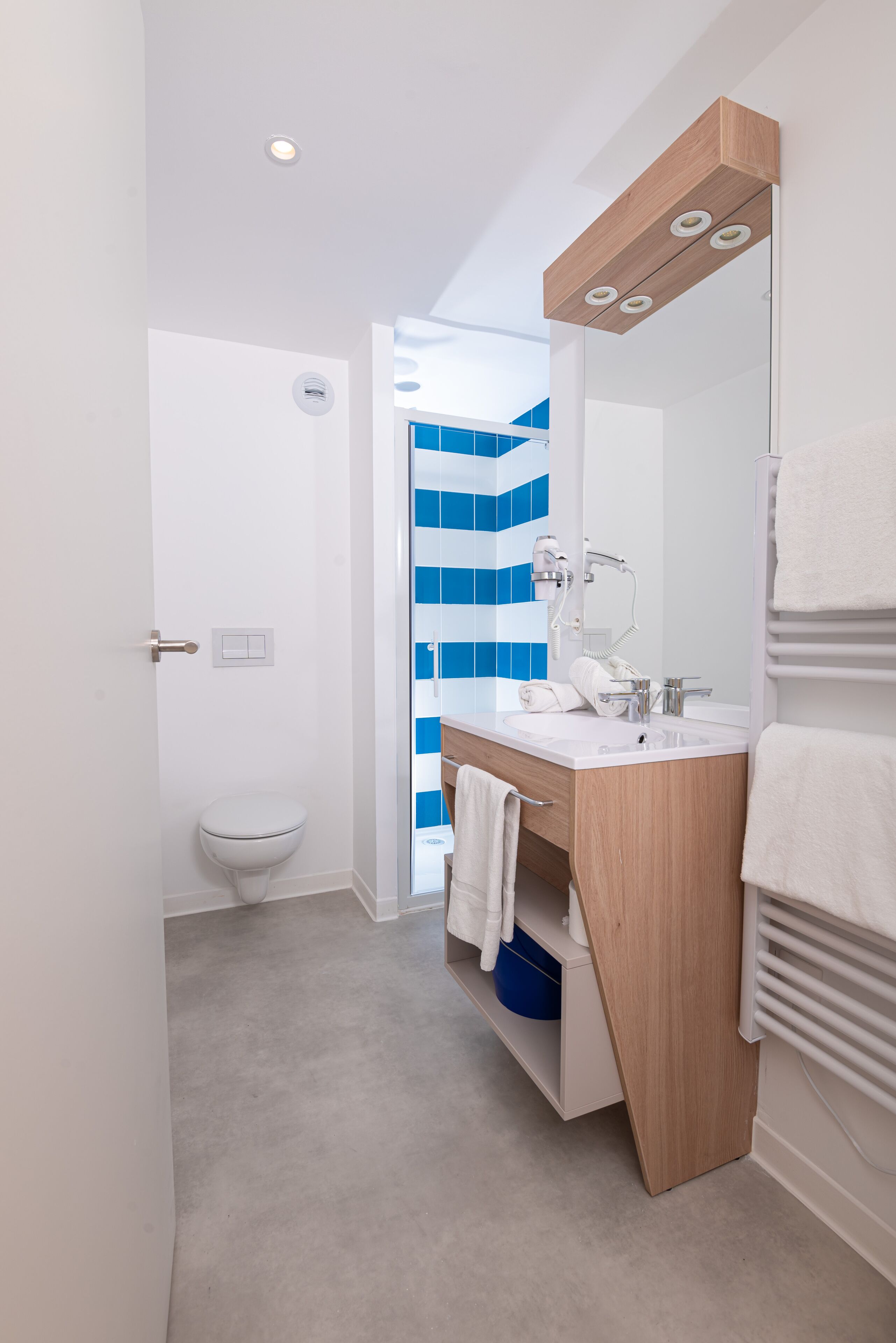 A modern bathroom with a white toilet, a wooden vanity with a mirror, and a blue-striped shower wall.
