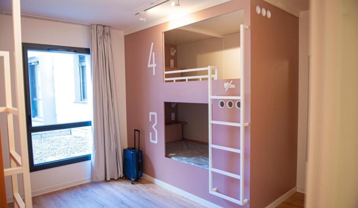 A room with bunk beds, a suitcase, and a window with curtains.