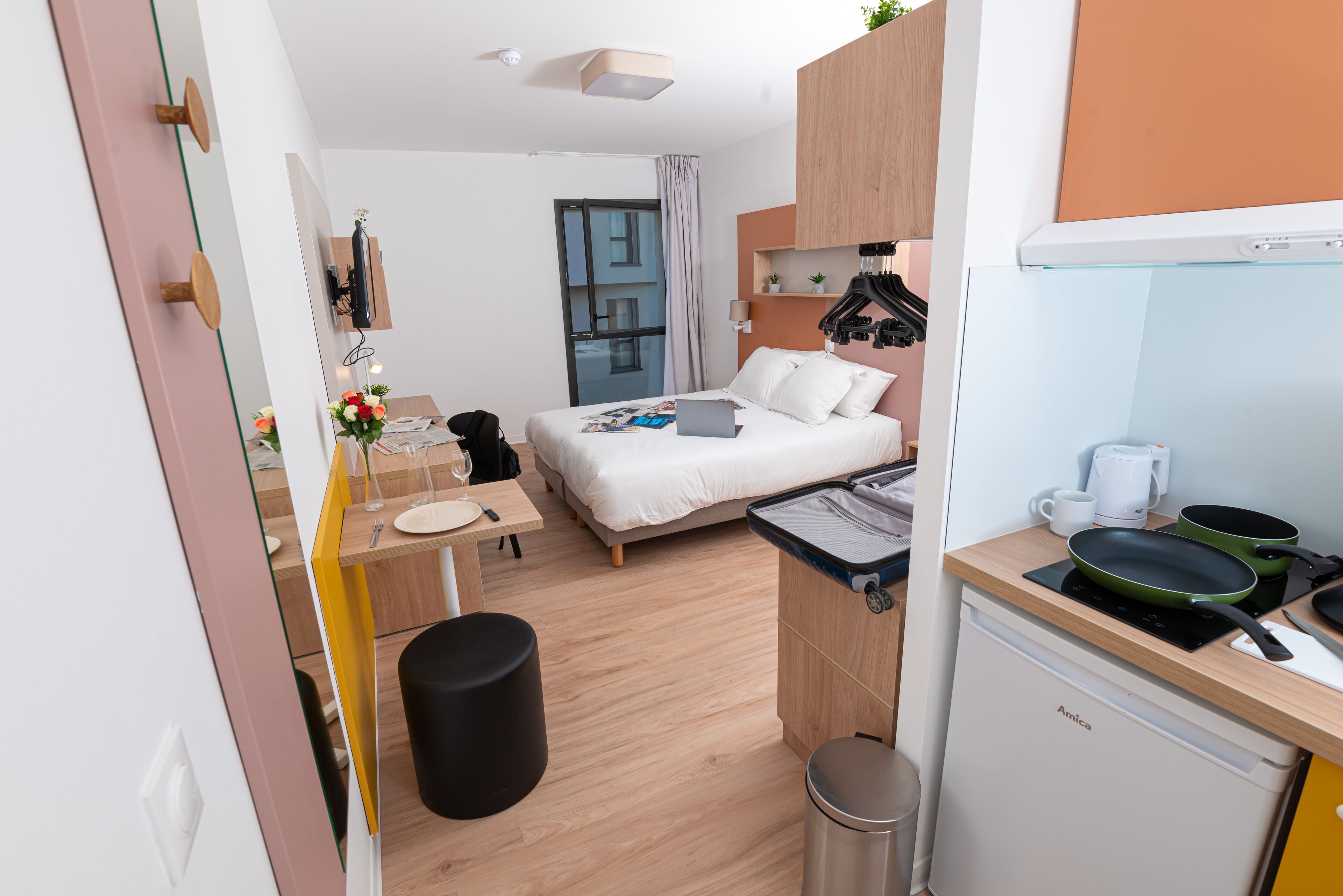 A compact hotel room with a bed, a small desk, a kitchenette, and a bathroom.