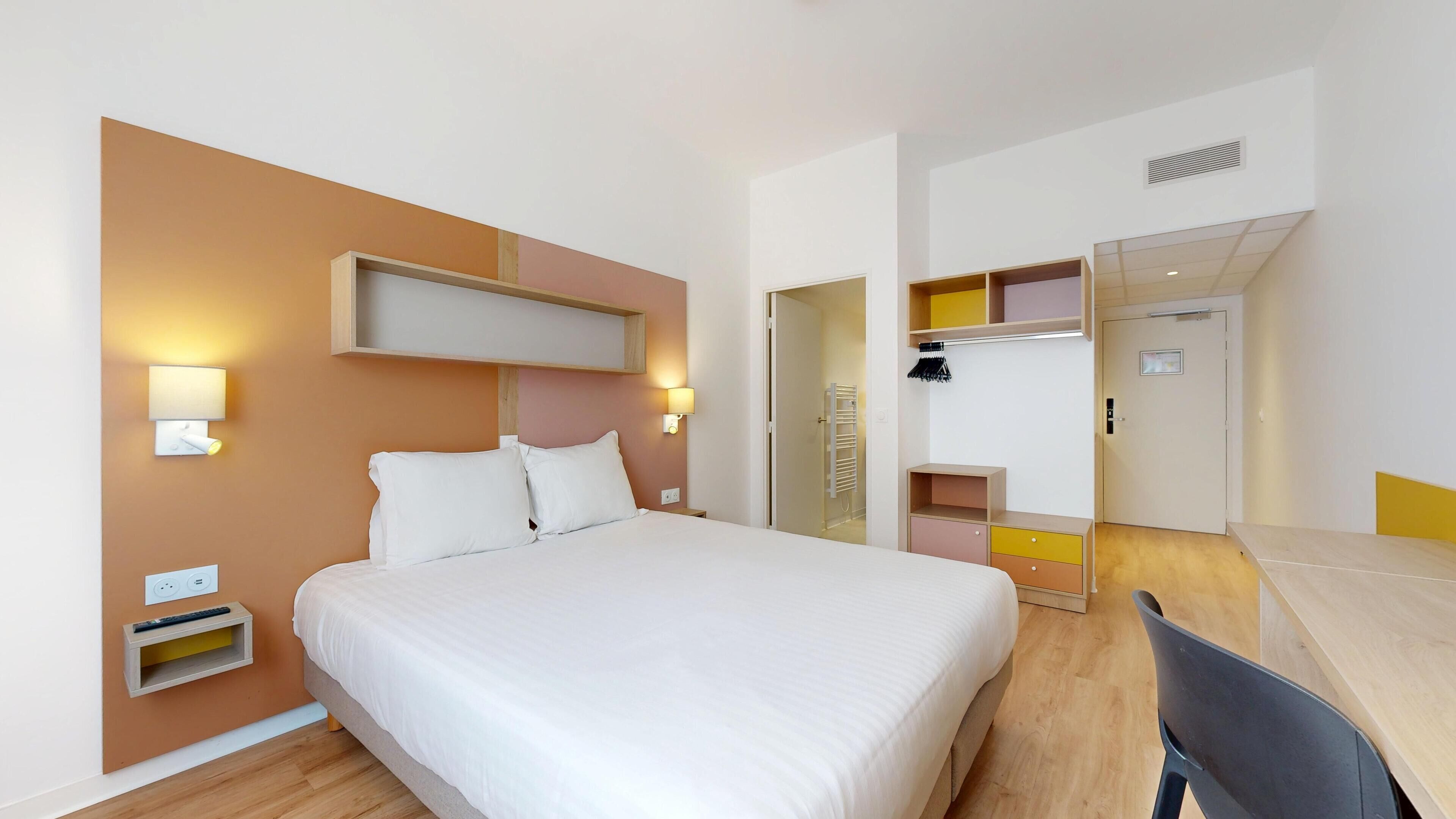 Una habitación de hotel con cama, mesitas de noche, un escritorio y una silla.