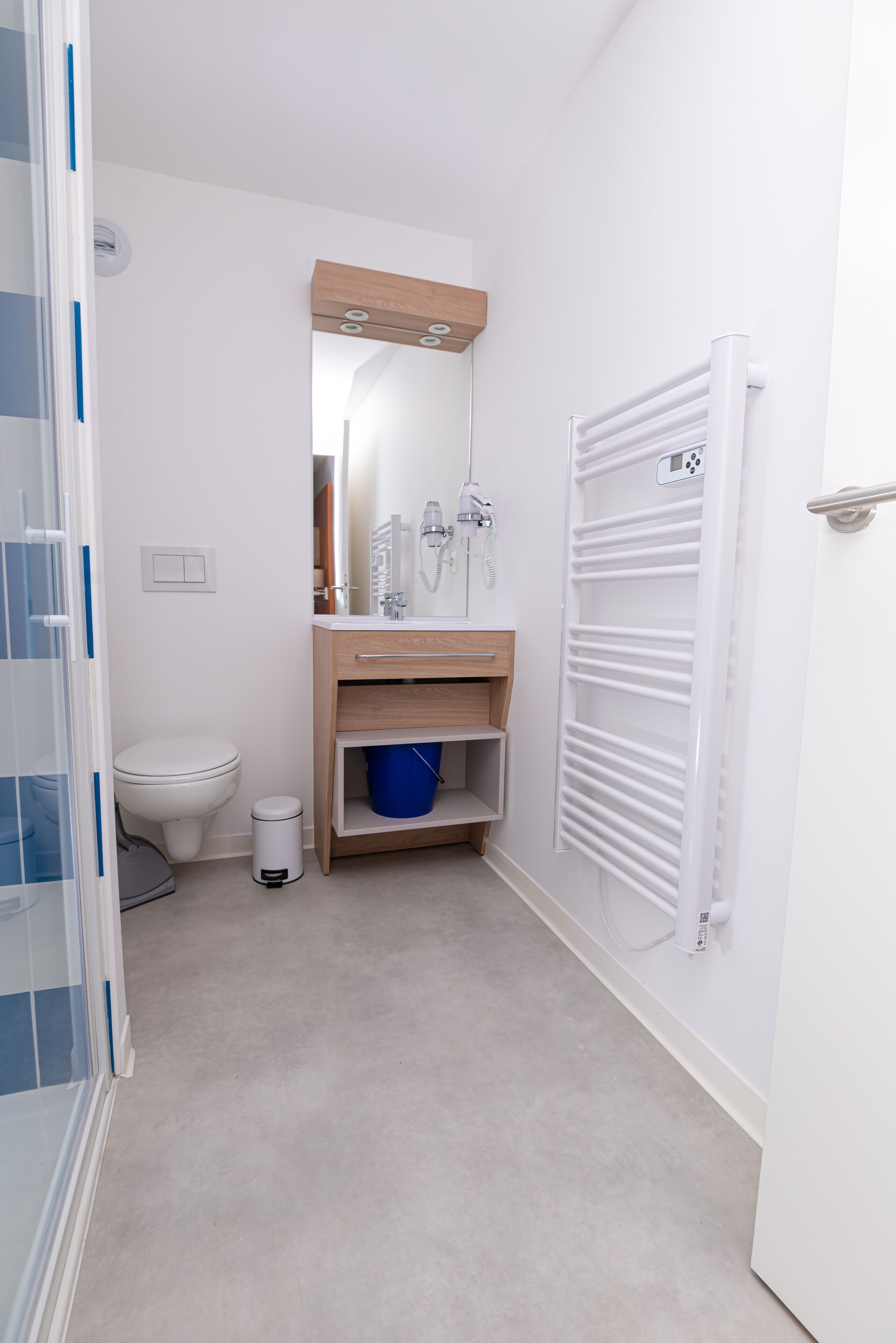 Ein kleines, schmales Badezimmer mit Toilette, Waschbecken mit Spiegel und Handtuchhalter.