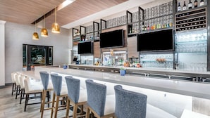 Een moderne bar met een lange toonbank, diverse zitplaatsen en een scala aan flessen en glazen op planken.