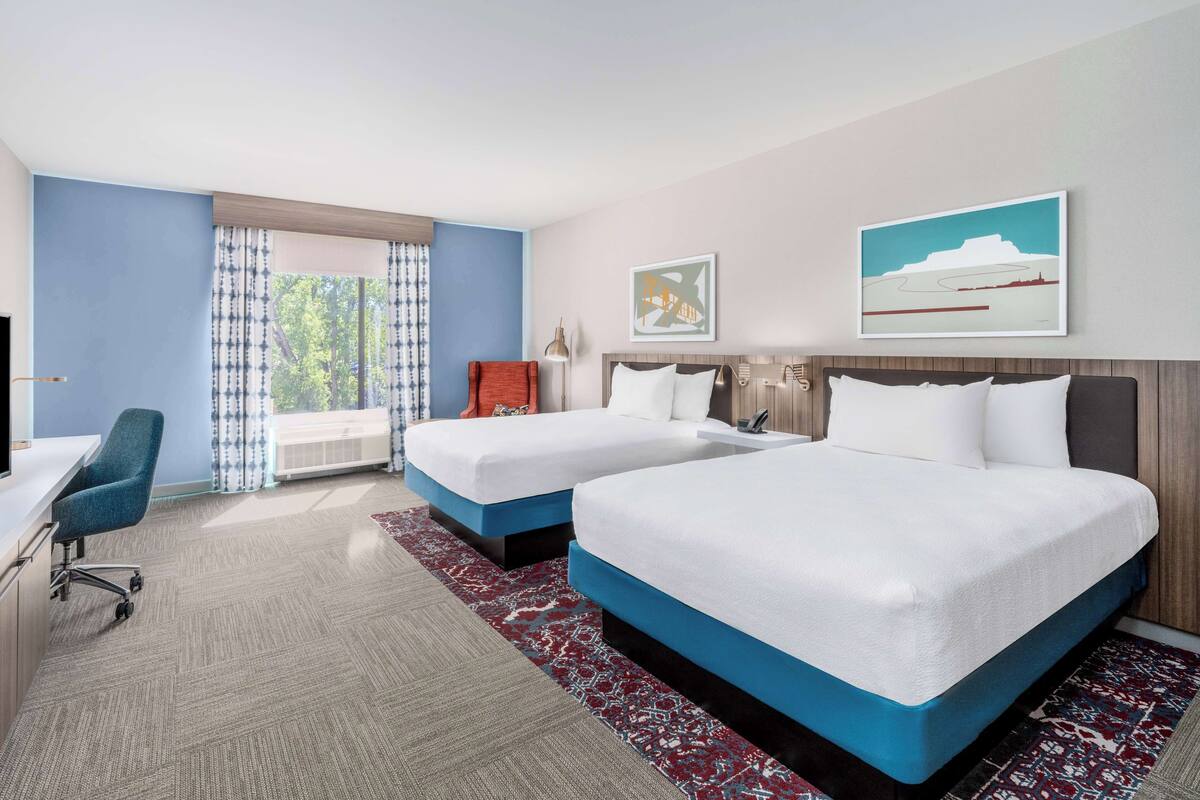 A hotel room with two beds, a desk, and a chair.
