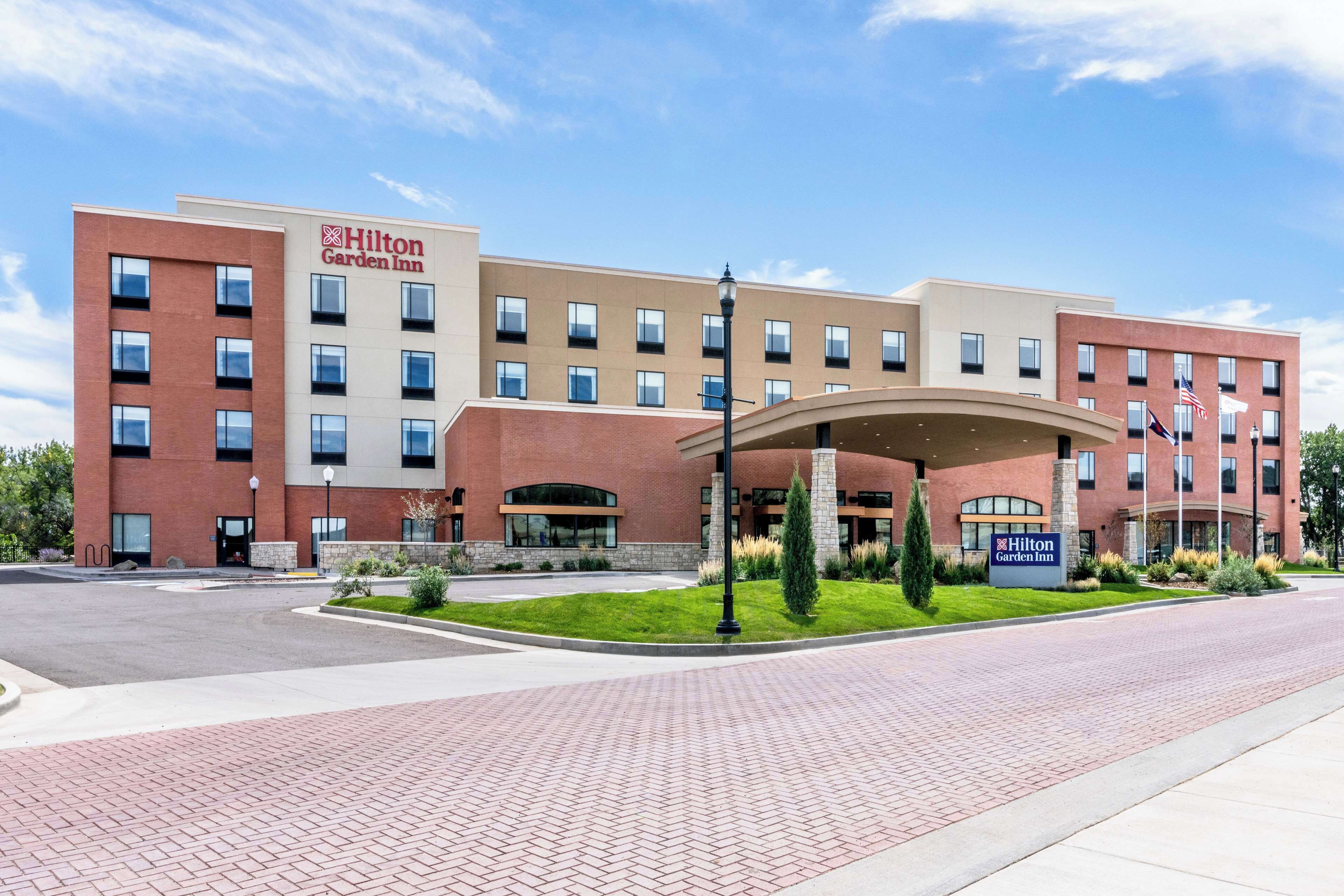 Um hotel Hilton Garden Inn com fachada de tijolos, diversas janelas e área de entrada com paisagismo.