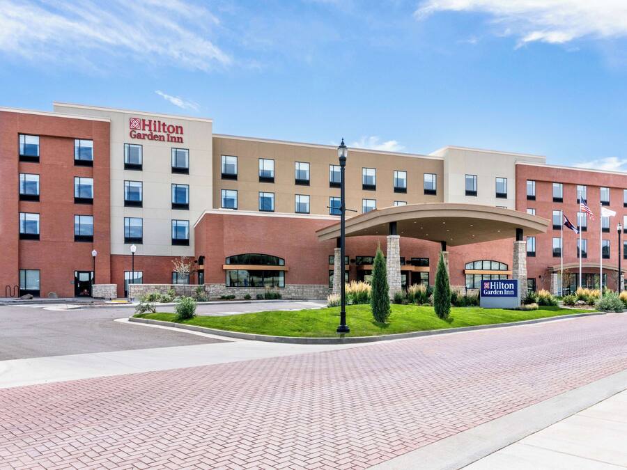 Um hotel Hilton Garden Inn com fachada de tijolos, diversas janelas e área de entrada com paisagismo.