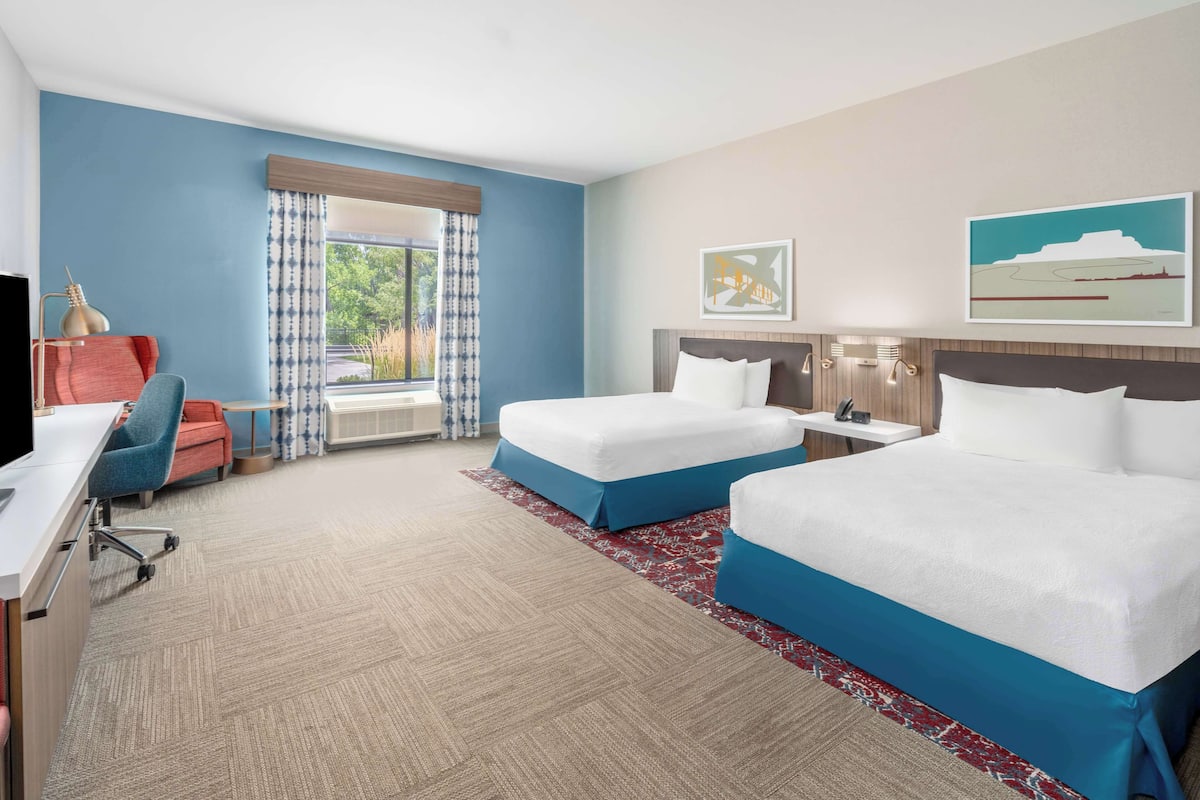 A hotel room with two beds, a desk, a chair, and a TV.