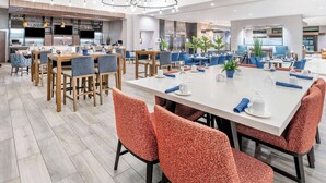 Een ruime eetruimte met meerdere tafels en stoelen, een bar met flessenkasten, en een moderne keuken op de achtergrond.