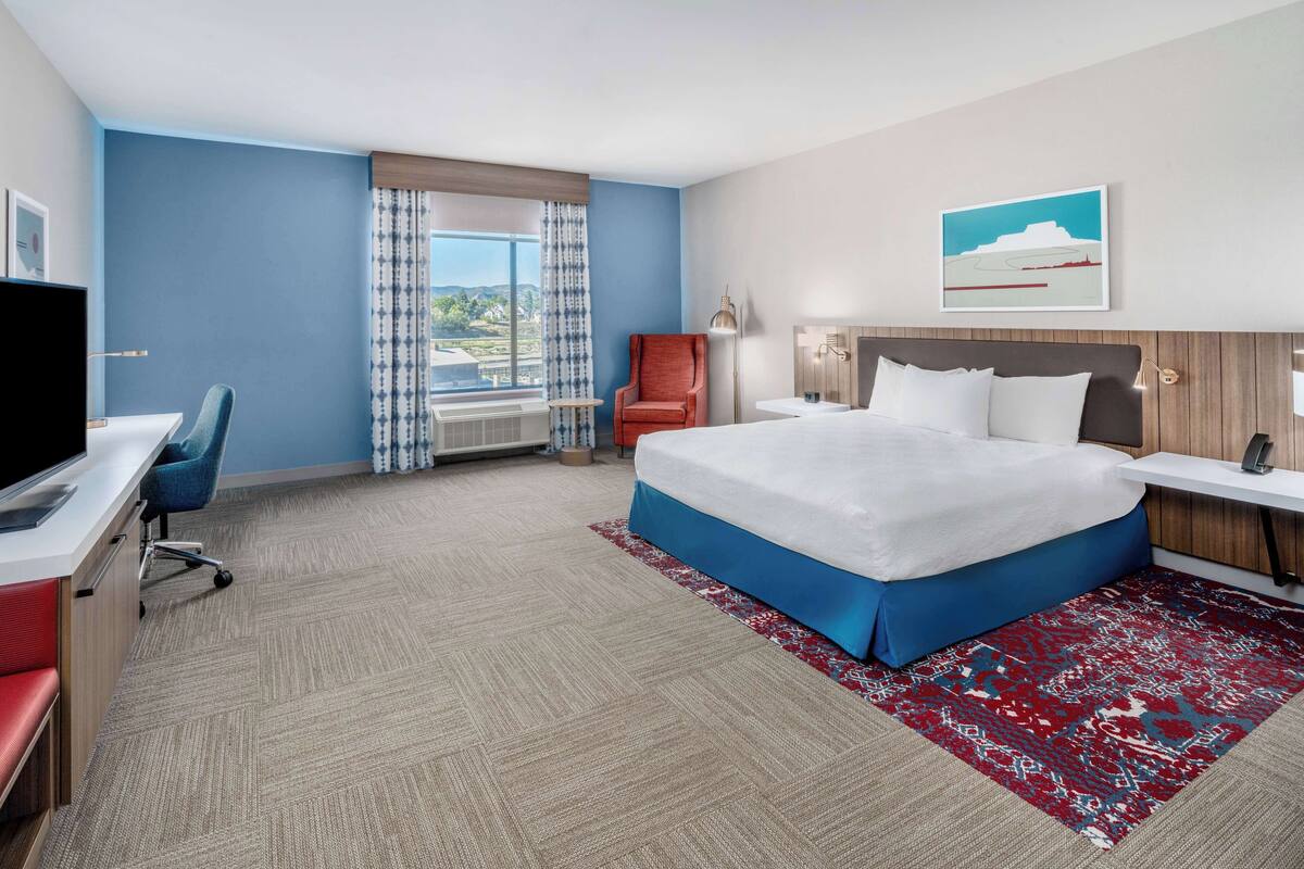 A hotel room with a large bed, a desk with a chair, a television, and a window with curtains.