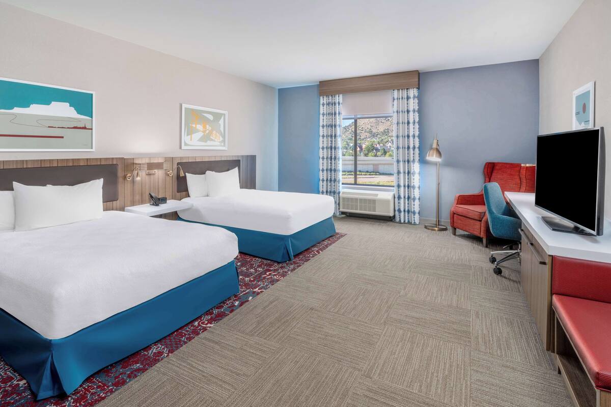 A hotel room with two beds, a desk with a TV, a chair, and a window with curtains.