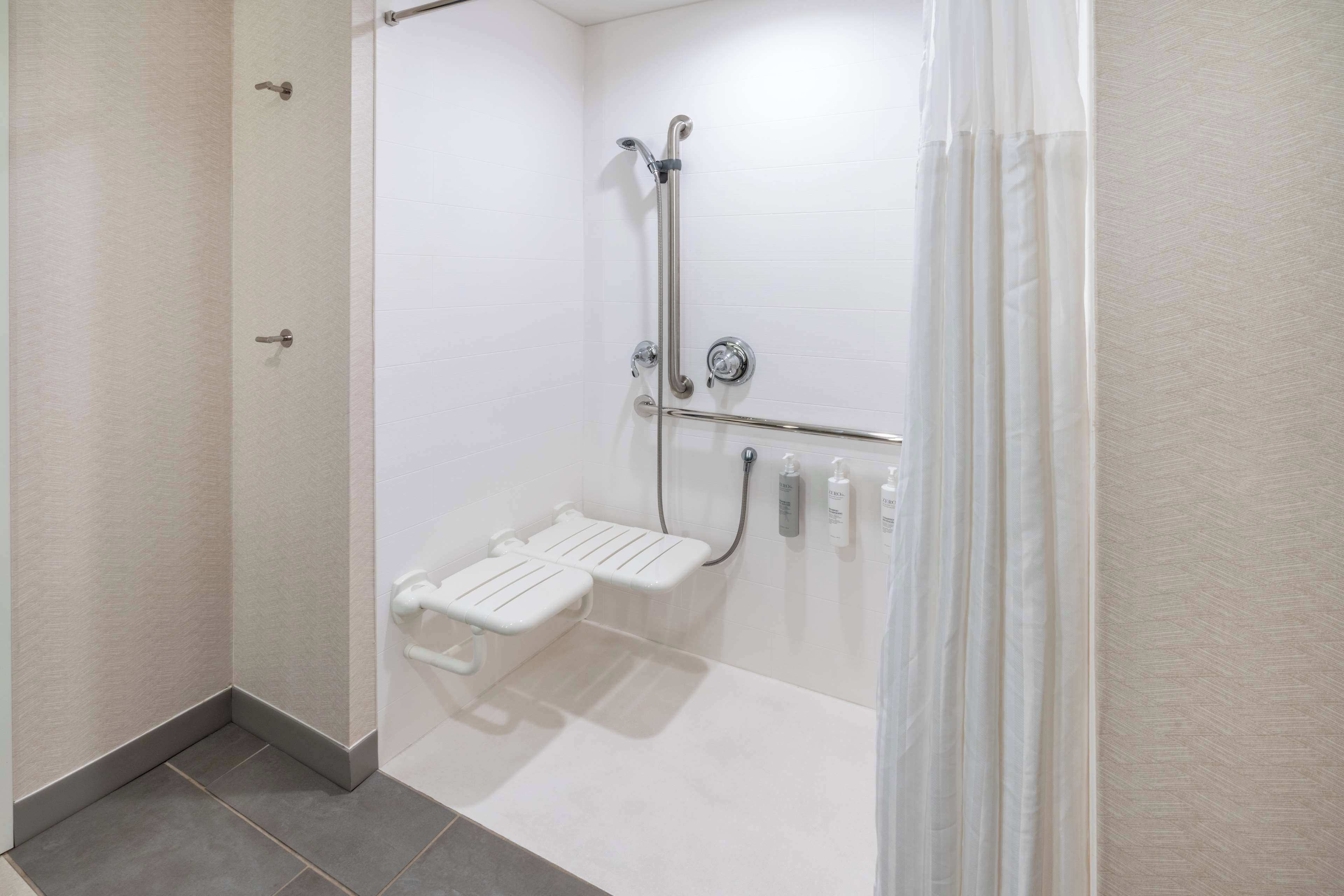 A modern bathroom with a walk-in shower, grab bars, and a handheld showerhead.