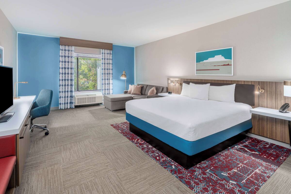A modern hotel room with a large bed, a desk, and a chair.