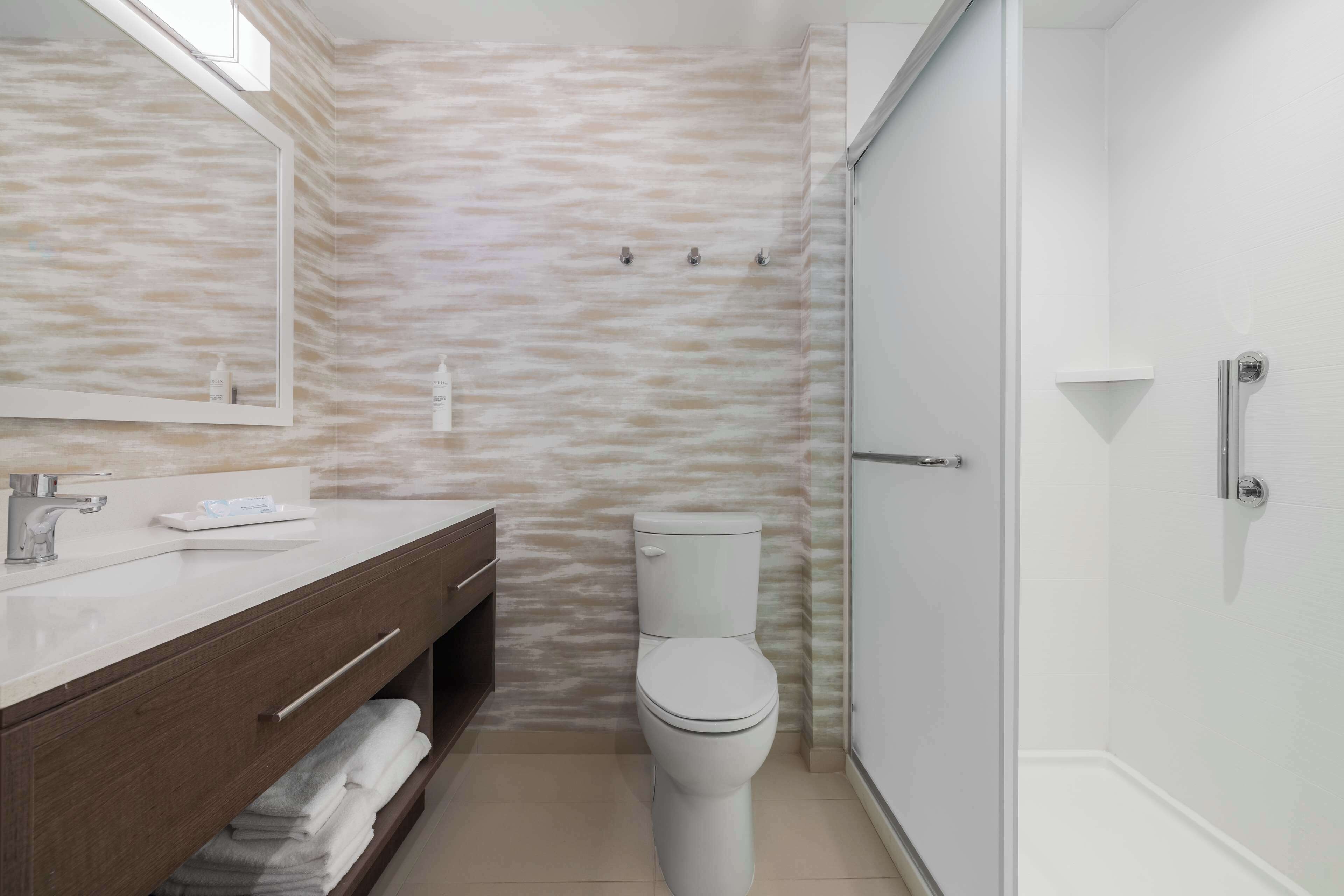 A modern bathroom with a marble-patterned wall, a white toilet, a vanity with a mirror, and a shower area.