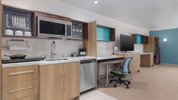 A modern kitchen with a microwave, stove, and dishwasher. There is a desk with a chair and a television.