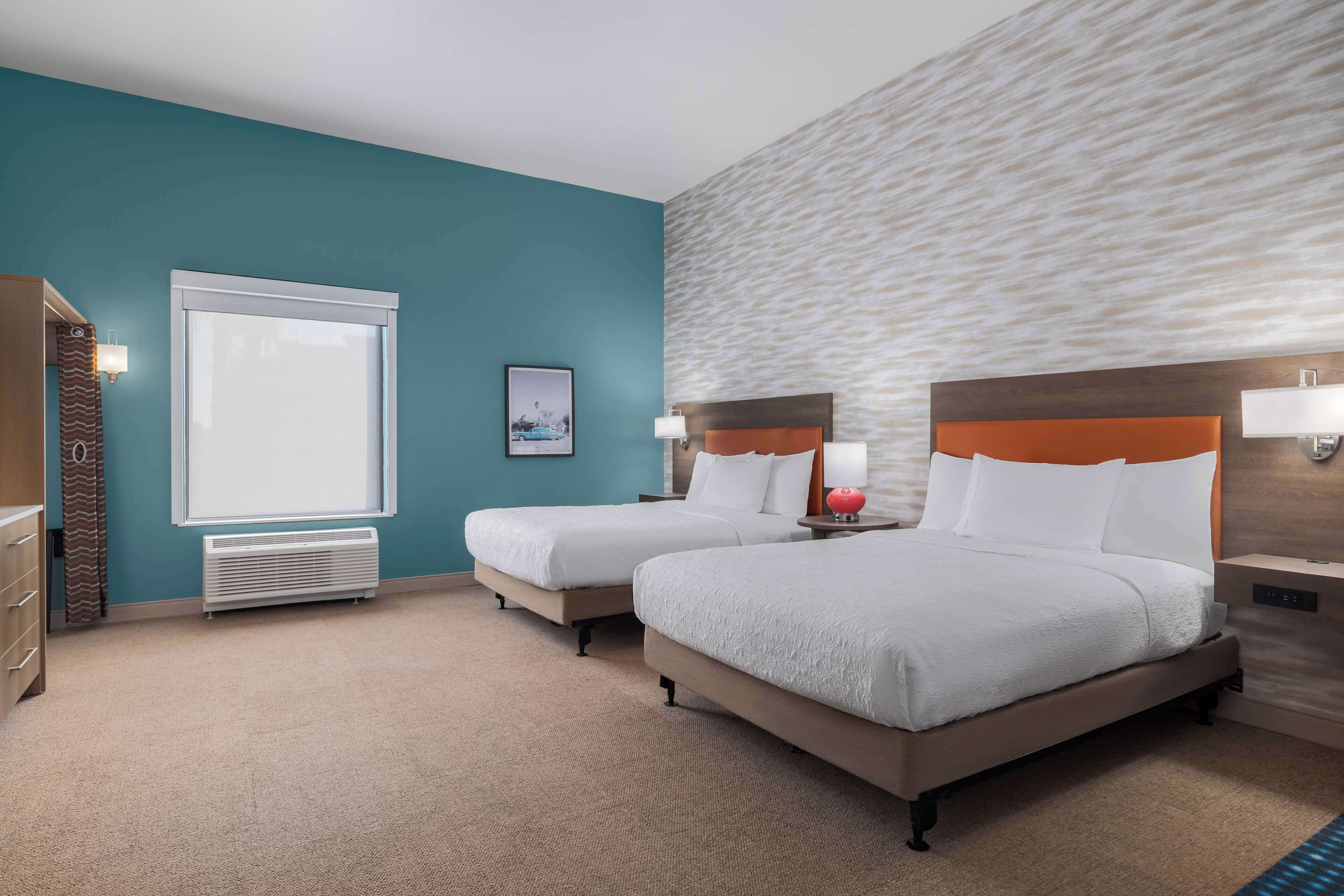 A hotel room with two beds, a large window, a wall heater, and a view of the city.