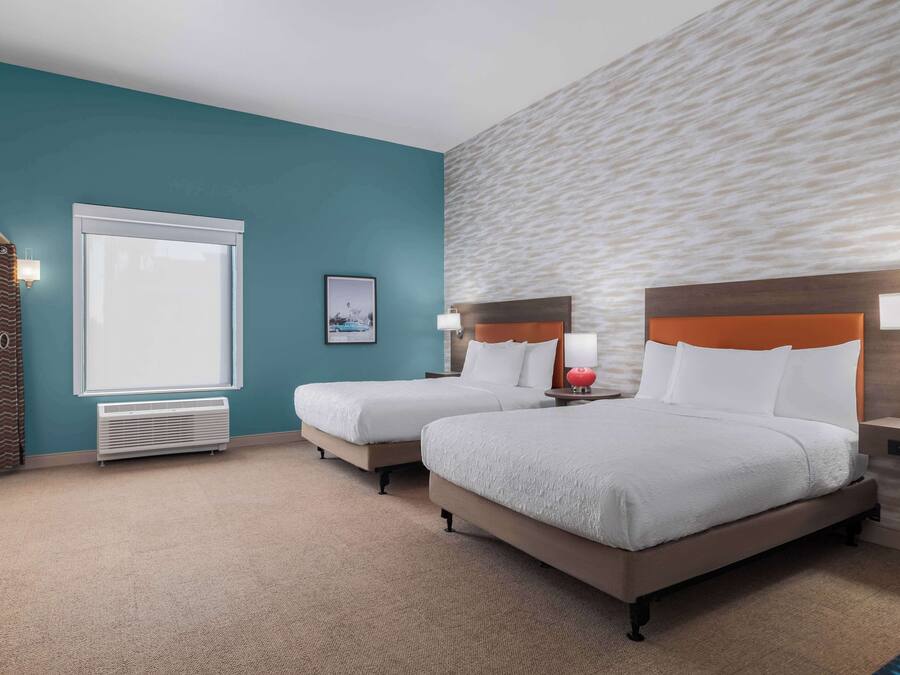 A hotel room with two beds, a large window, a wall heater, and a view of the city.