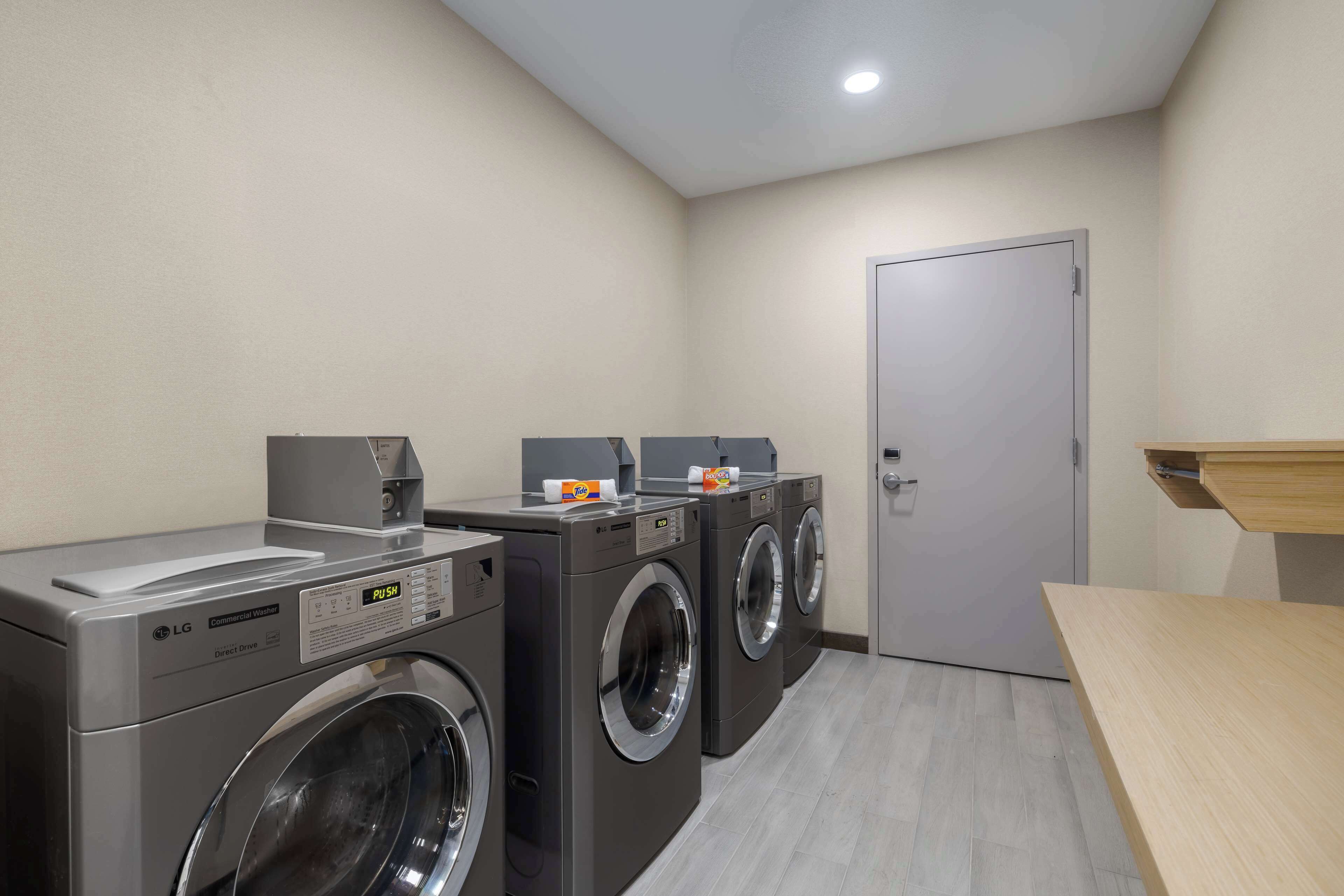 A laundry room with two front-loading washing machines, a dryer, and a door.