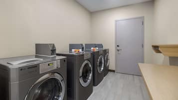 A laundry room with two front-loading washing machines, a dryer, and a door.