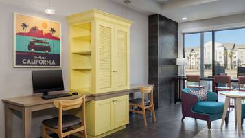 Une chambre d’hôtel moderne avec un bureau en bois, une armoire jaune, un fauteuil turquoise et une grande fenêtre donnant sur la ville.