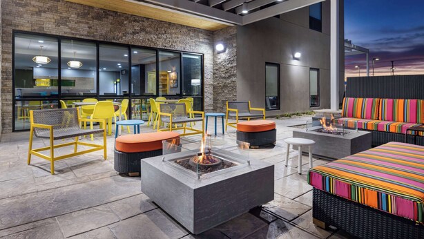 An outdoor seating area with a fire pit, yellow and blue chairs, and a colorful sofa. - Home2 Suites By Hilton El Centro (El Centro)