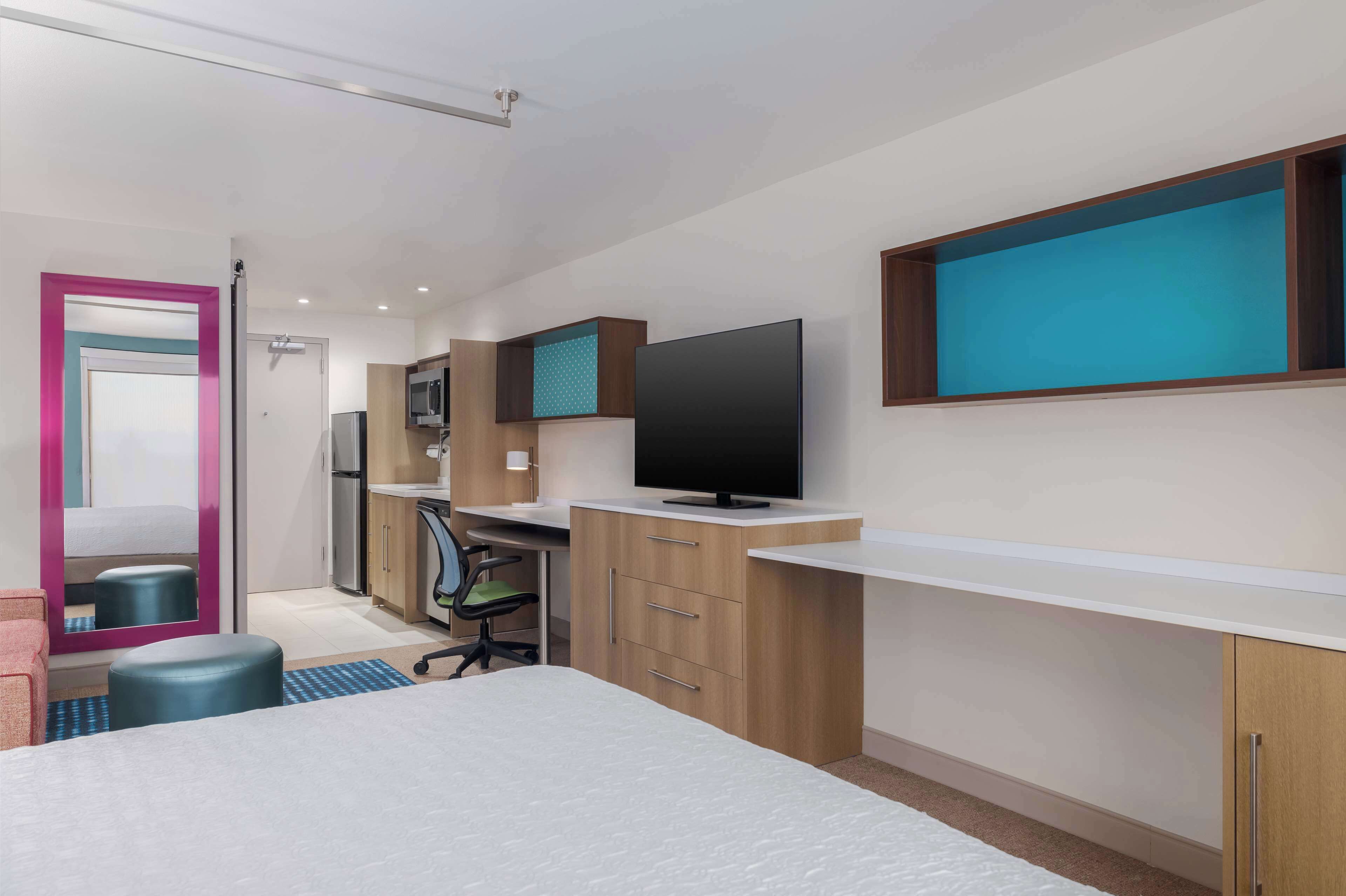 Ein modernes Hotelzimmer mit Bett, Schreibtisch, Fernseher und einer Küchenzeile.