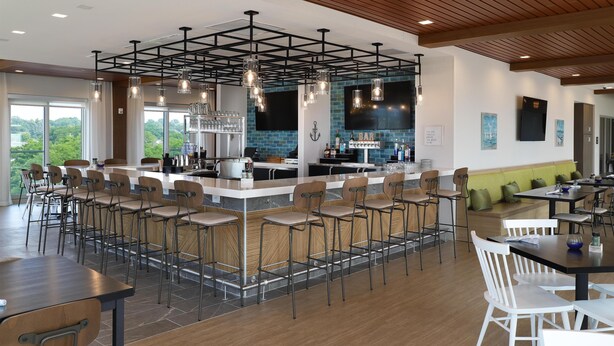 A modern bar area with a central island, bar stools, and a seating area with tables and chairs. - Hampton Inn & Suites Manistee Waterfront (Manistee)