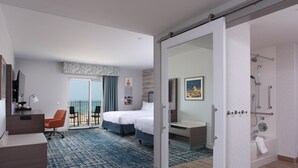 A hotel room with a bed, a desk, a chair, a bathroom with a shower, and a balcony with a view. - Hampton Inn & Suites Manistee Waterfront (Manistee)
