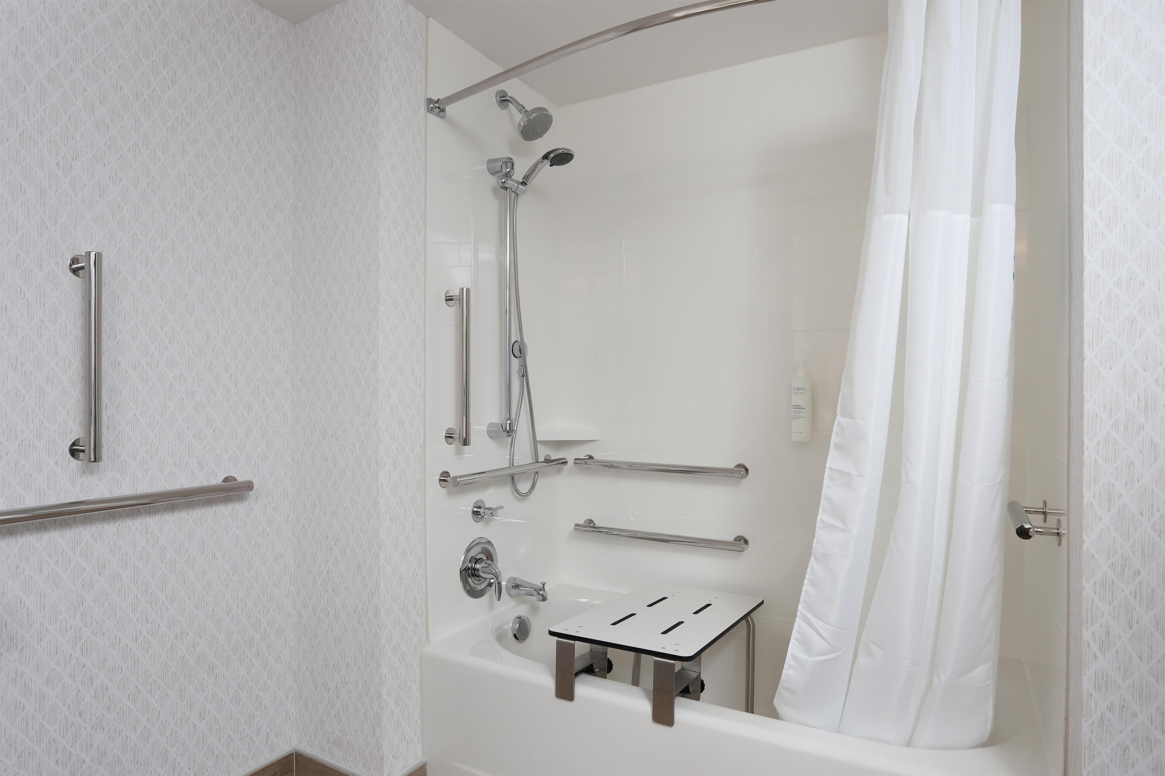 A shower area with a bathtub, grab bars, and a showerhead.