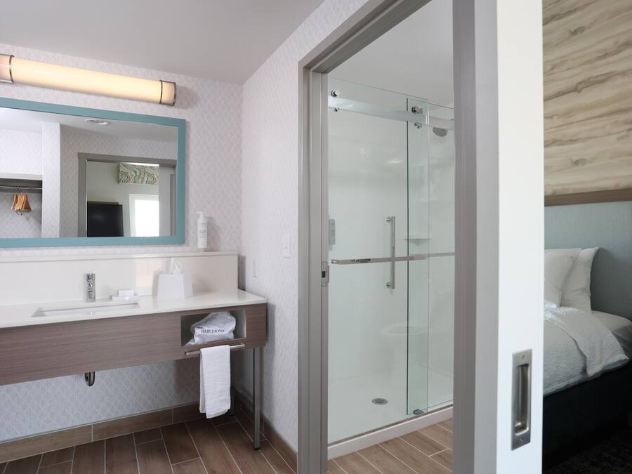 A modern bathroom with a large mirror, a sink, and a glass-enclosed shower.