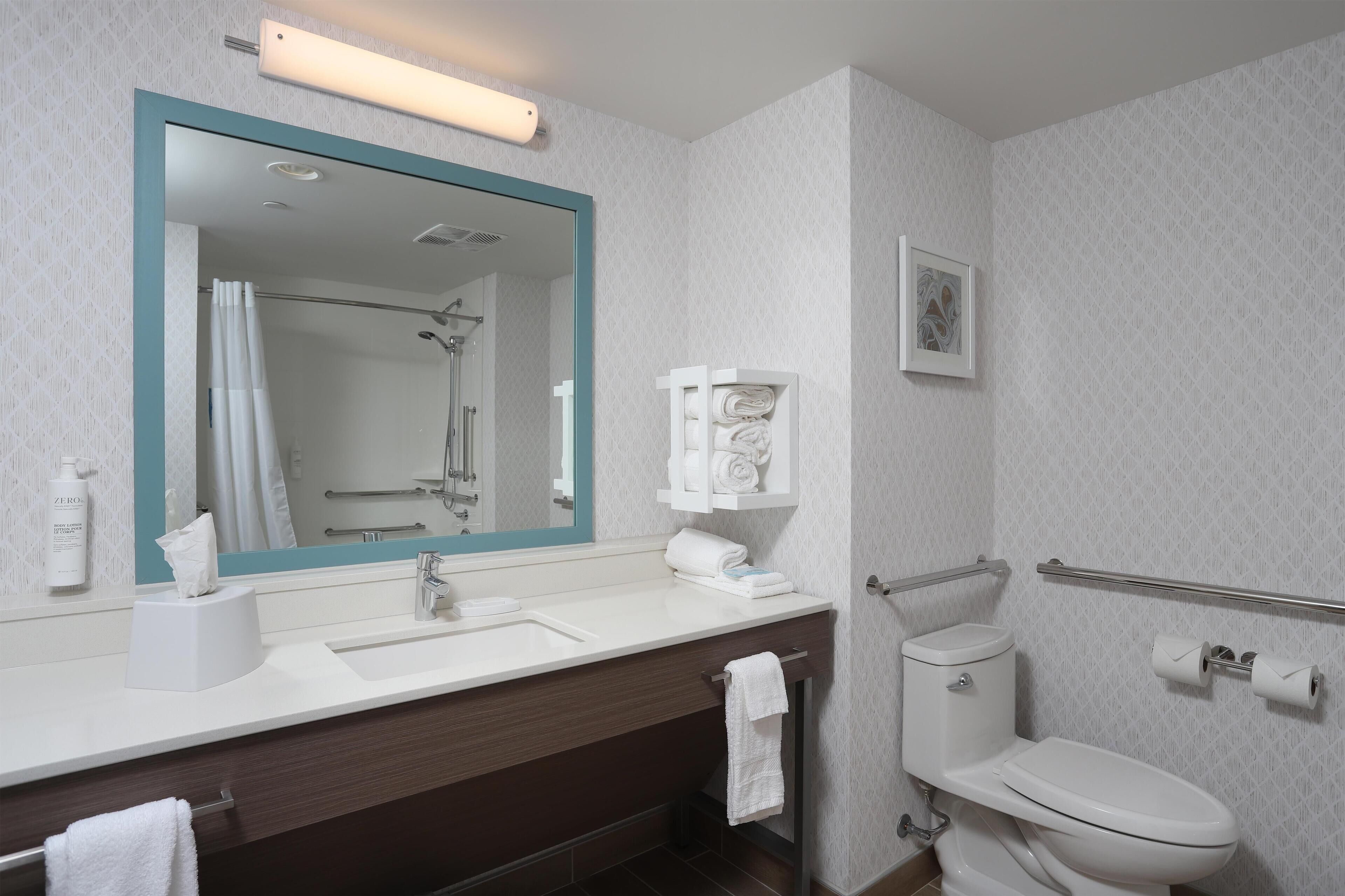 A modern bathroom with a large mirror, white sink, and a toilet.