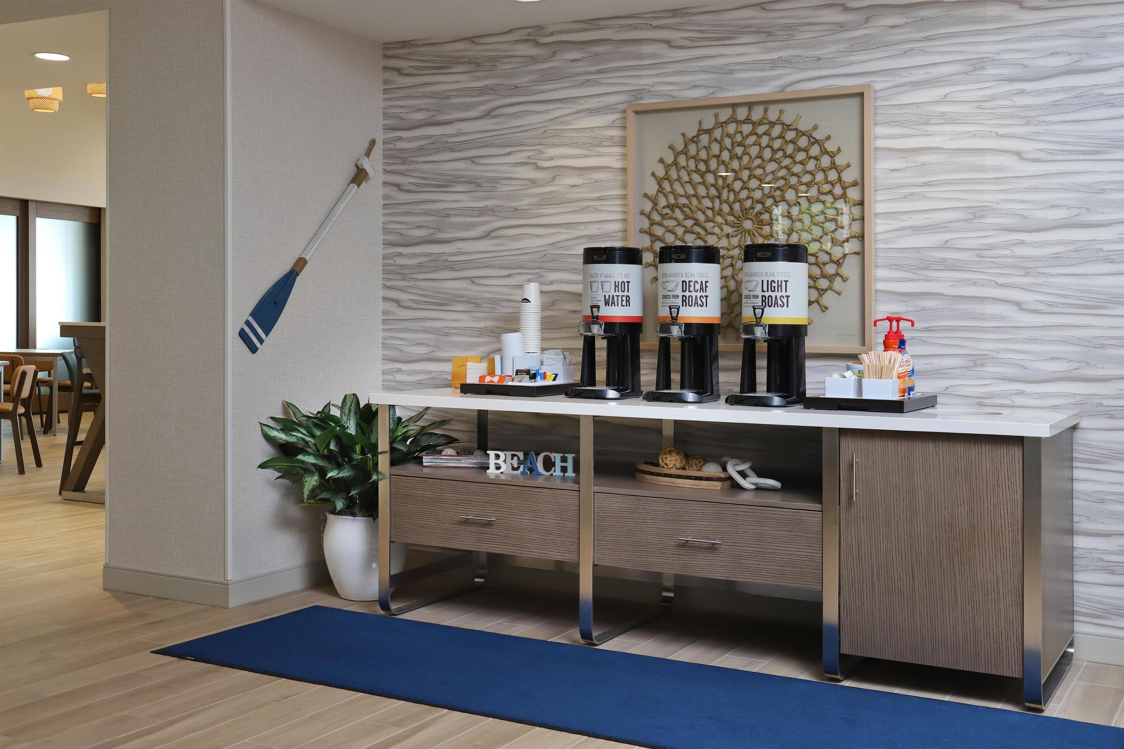 A modern reception desk with a marble wall backdrop, a framed artwork, and a coffee station with labeled dispensers.