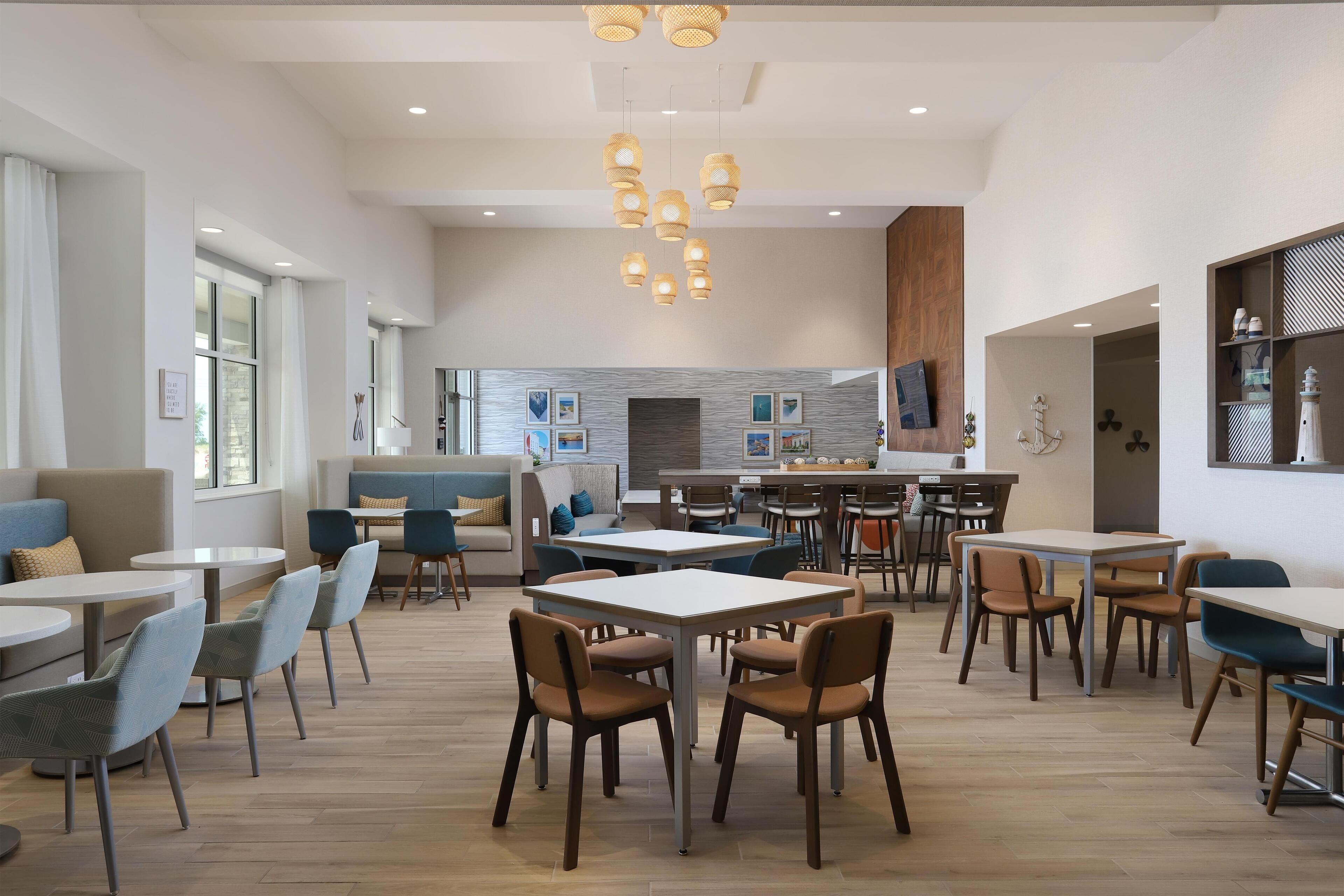 Un comedor moderno con mesas y sillas redondas, una cocina al fondo e iluminación colgante.