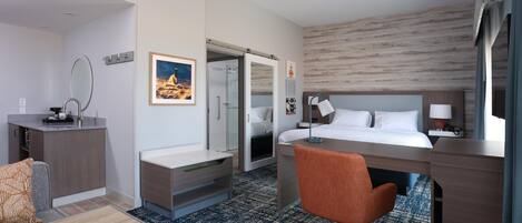 Ett hotellrum med en säng, ett skrivbord, en stol och ett litet pentry.