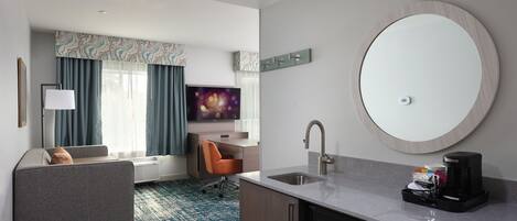 Una habitación de hotel moderna con sofá, televisor, cafetera y lavamanos.