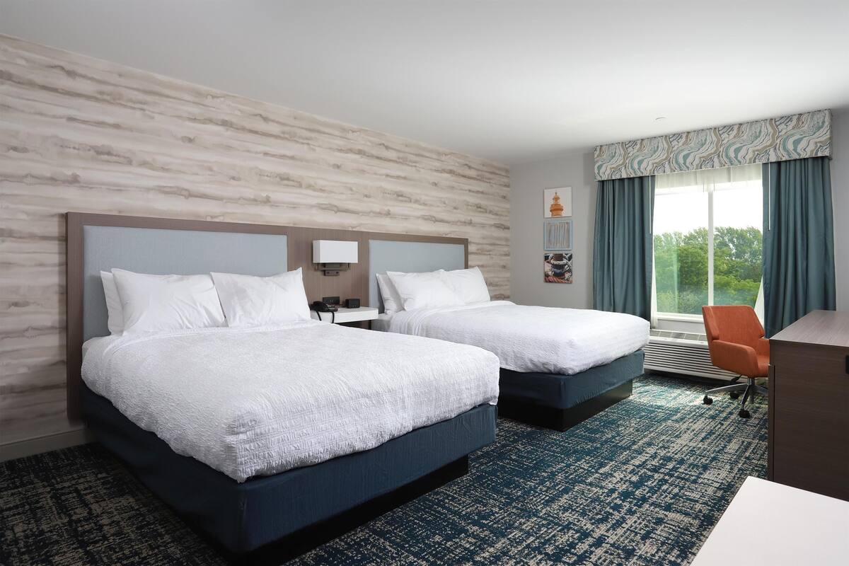 A hotel room with two beds, a desk, and a chair.