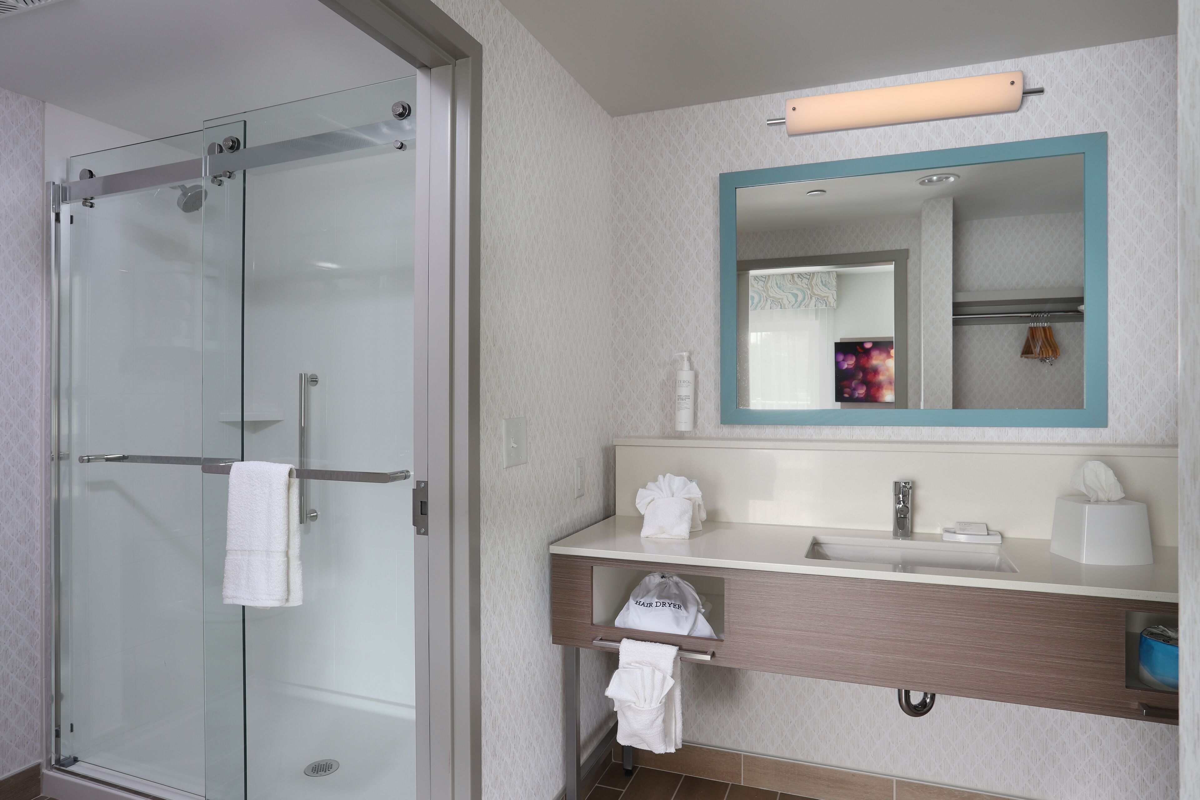 Een moderne badkamer met een douchecabine van glas, een wastafel met spiegel en een handdoekrek.