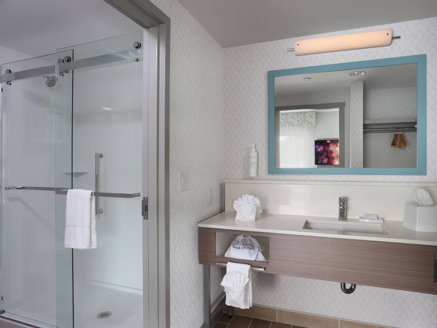 Een moderne badkamer met een douchecabine van glas, een wastafel met spiegel en een handdoekrek.